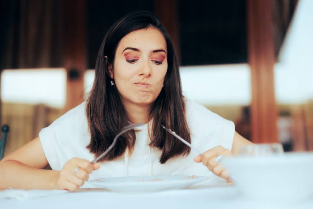 Woman looking unsure at her plate with a fork and knife in her hands.