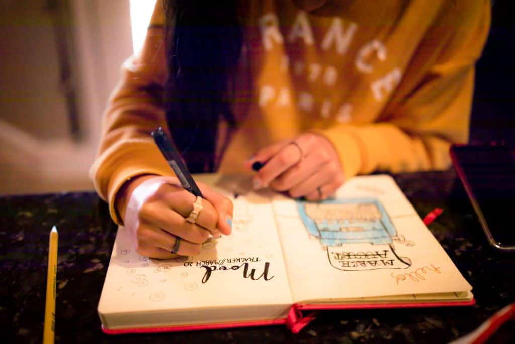 Young woman with a yellow sweatshirt writes in her journal.