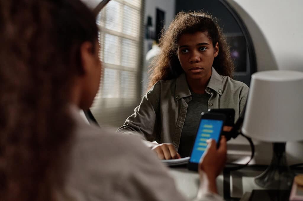 Young African American girl holding her smartphone and gazing pensively into the mirror